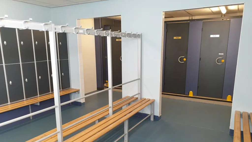 Changing room with benches, pegs and cubicles.