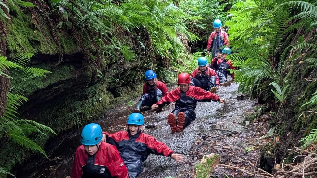 Children with helmets and protective gear sliding down a river.