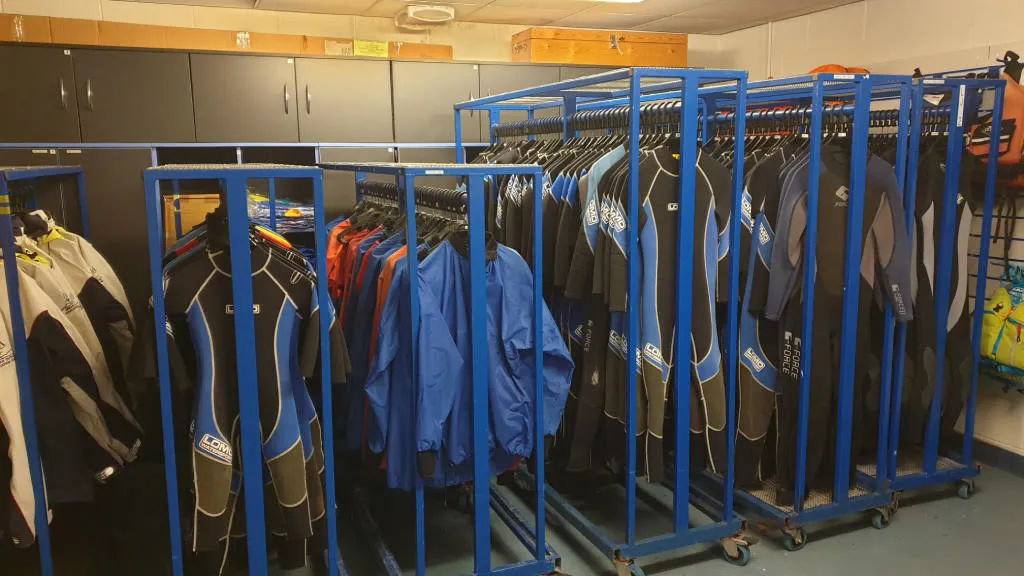 Several rows of wetsuits and outerwear hanging up drying.