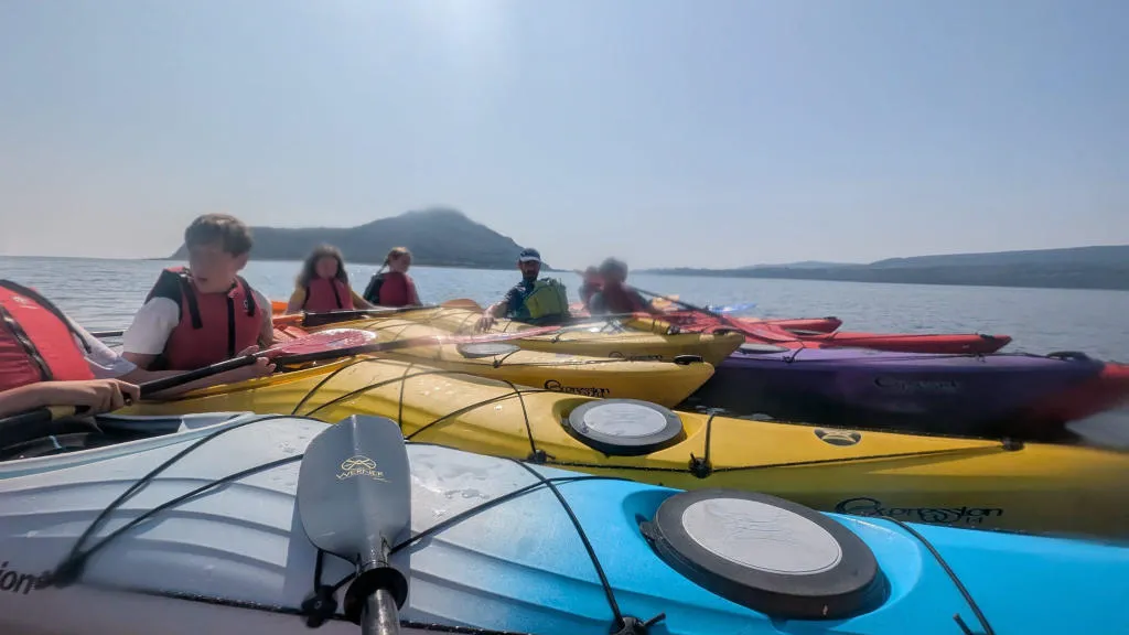 group of people in kayaks in the sea with the holy isle in the background.