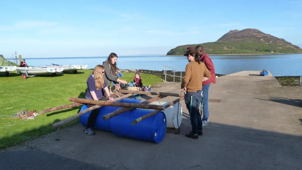 group making a raft with large tree branches and barrels.