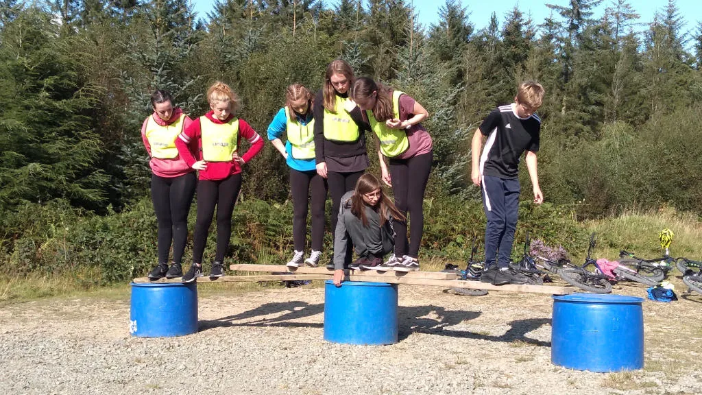 A group of children playing game as a team to stay balanced on top of barrels.